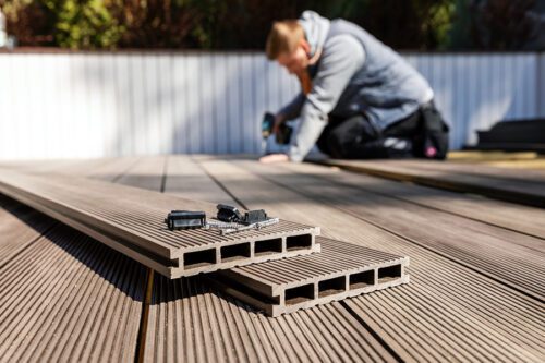 Close-up of composite decking boards and screws, with a person installing decking in the blurred background.