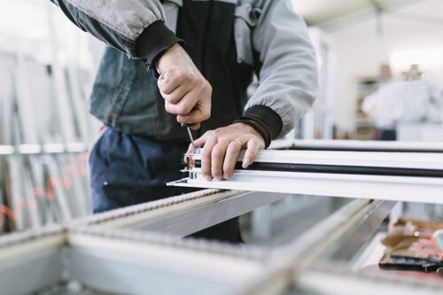 A person uses a screwdriver to assemble or adjust a metal frame in a workshop setting.