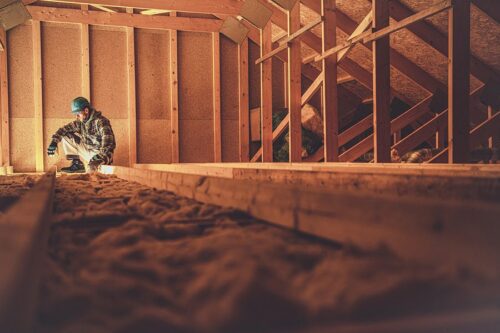 Un ouvrier portant un équipement de sécurité utilise une lampe de poche pour inspecter ou travailler dans un grenier en bois en cours de construction.